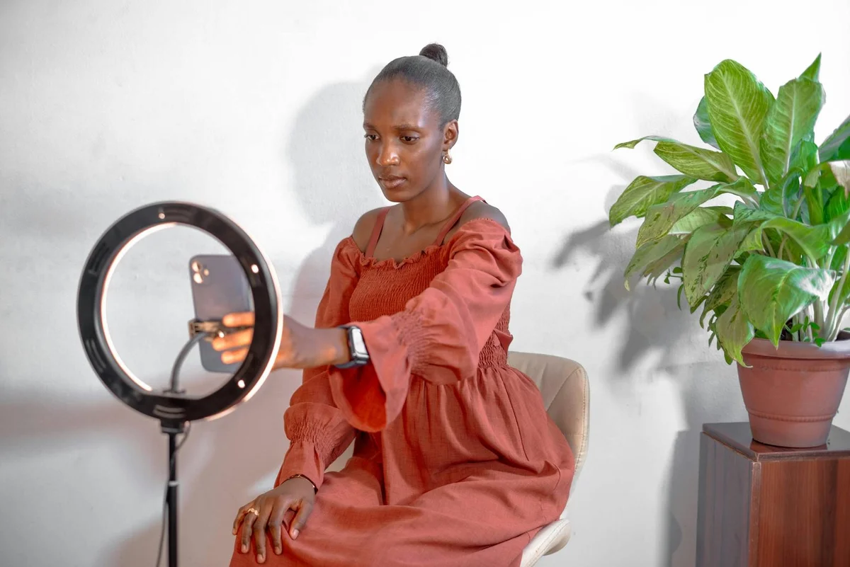 A young woman uses a smartphone ring light setup for vlogging from home.