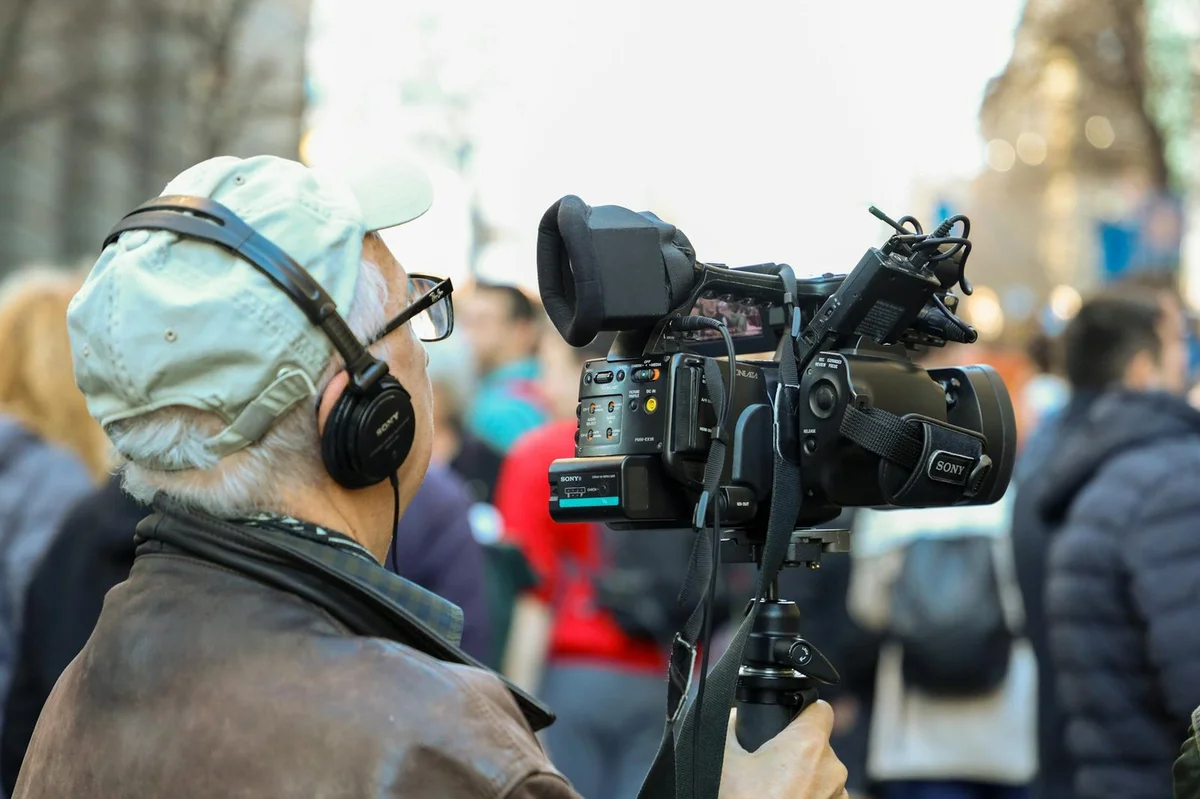 A cameraman records an urban event with professional equipment in a bustling cit