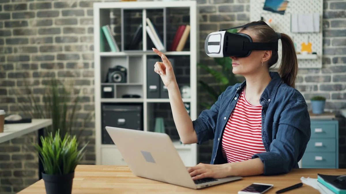 A woman using a VR headset while working on a laptop, exploring virtual reality