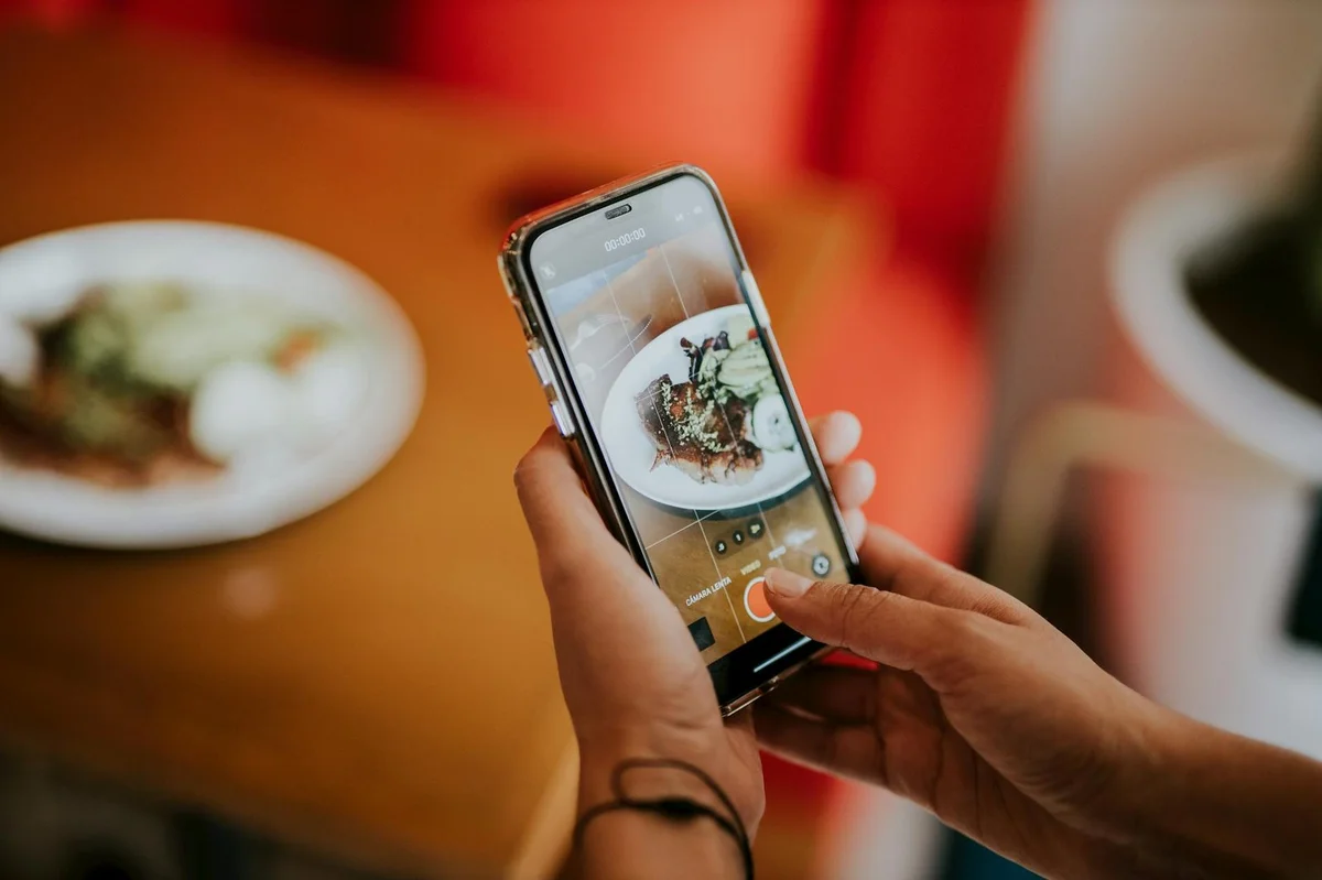 Close-up of a person using a smartphone to photograph food in a cozy indoor sett