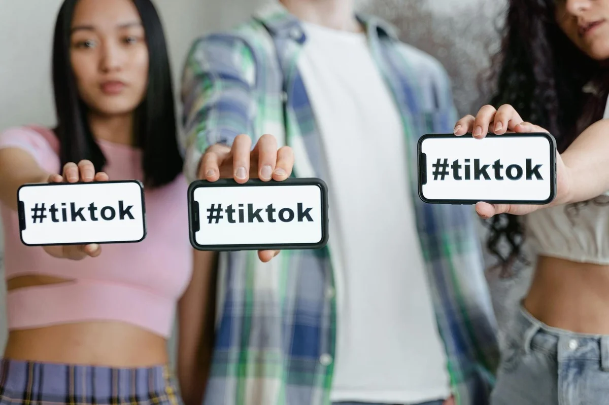 Young adults holding smartphones with TikTok hashtag, showcasing social media en