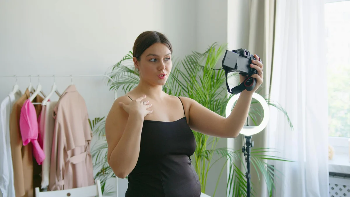 Algoritmo de TikTok 2026: cómo funciona realmente y qué busc... — A young woman records a vlog indoors with a camera, surrounded by stylish clothi