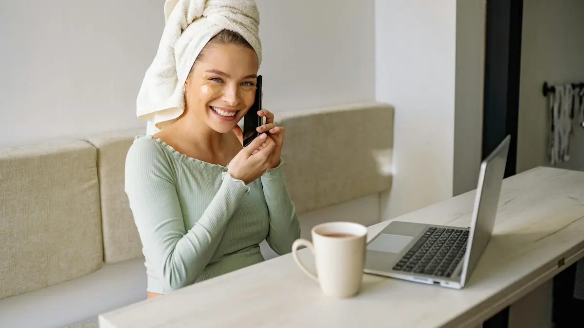 Caucasian woman multitasking with phone and laptop, embracing remote work and self-care. Smiling and