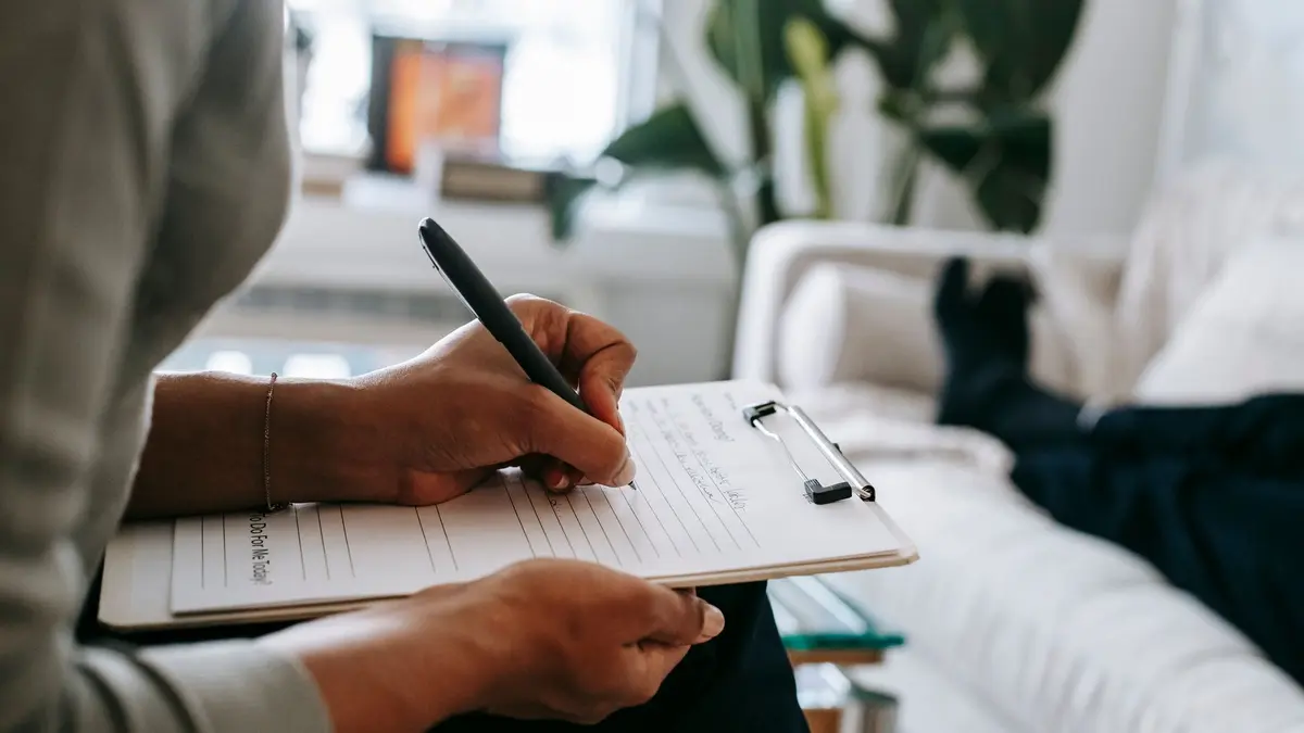 Unrecognizable ethnic female therapist taking notes on clipboard while filling out form during psych