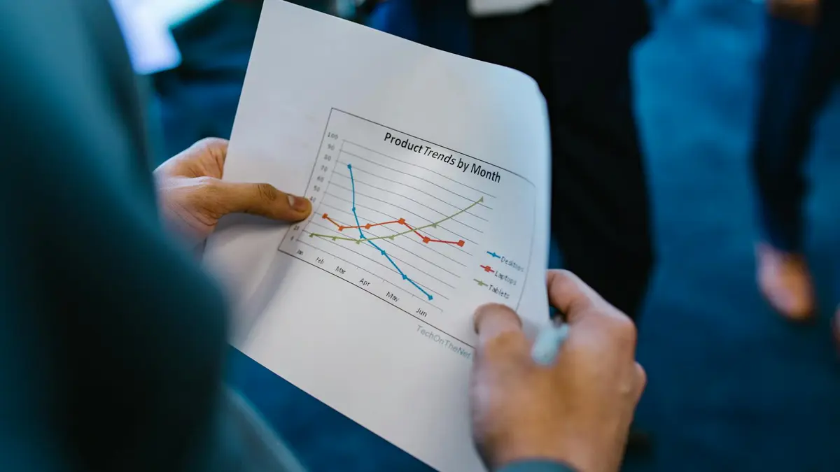 Close-up of hands holding a paper with a line graph showing product trends by month during a busines