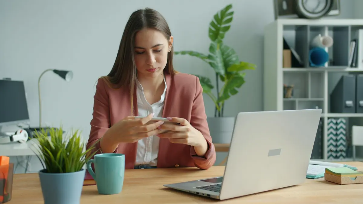 Businesswoman checking her phone while at her desk in a modern office setting.
