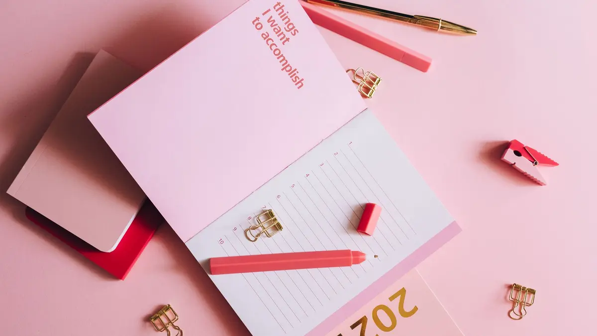 Organized workspace with pink planner, pen, and clips on pastel background.